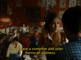 Movie gif. Rosamund Pike as Elspeth in Saltburn. She's standing in a room full of people who are sprawled on the floor and she looks utterly pleasant and endearing as she smiles and says, "I have a complete and utter horror of ugliness ever since I was very, very young. I don't know why."