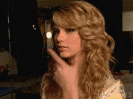 Celebrity gif. Taylor Swift caresses her chin before smiling subtly.