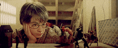 Movie gif. A bored Daniel Radcliffe as Harry Potter plays dully with toys in his room under the stairs.