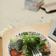 A kitten reaching a paw toward a plate of leafy salad on a table