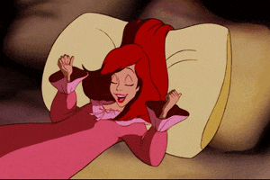 Disney gif. In human form, Ariel from the Little Mermaid stretches out in bed and rolls onto her side, nuzzling into a fluffy pillow.
