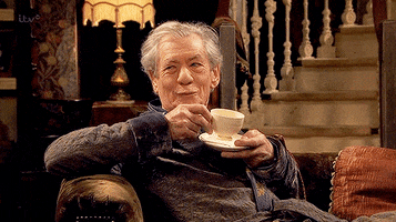 TV gif. In a dark bathrobe, Ian McKellen as Freddie Thornhill in Vicious smiles smugly from his cozy seat on the sofa before returning to his white teacup.