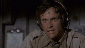 Video gif. Sweat pours off a stressed airplane pilots head as he wipes a hand across his wet brow. 