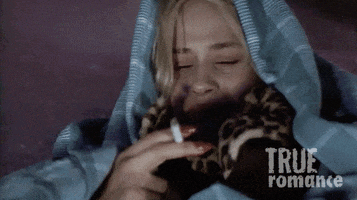 Movie gif. Patricia Arquette as Alabama Worley in True Romance has a blanket wrapped around her and covering her head. She has tear filled eyes as she smokes her cigarette sadly.