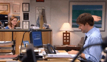 The Office gif. John Krasinski as Jim and Jenna Fischer as Pam sit in their respective desks and send one another a simultaneous air five, both grinning secretly.