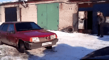 Video gif. A man walks toward an old red car in the snow. He kicks the front bumper and the bumper, a door, a headlight, and several other pieces fall off. He stops and stares in surprise.