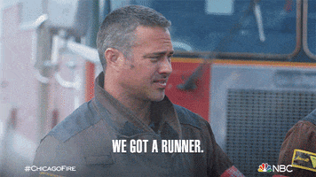 TV gif. Taylor Kinney as Kelly in Chicago Fire. Steam billows around him as he squints his eyes and tells the squad, "We got a runner."