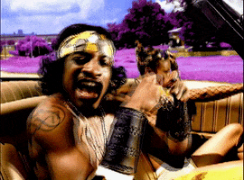 Music video gif. Andre 3000 in Outkast's B.O.B. (Bombs Over Baghdad), rides in a car, dancing and singing, while a woman sits with her hand on the wheel next to him. 