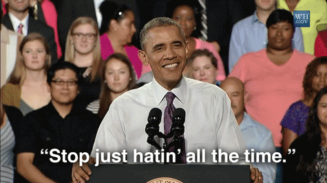 [Image description: A brown man, wearing a white shirt and purple tie standing at a podium with a crowd behind him. He is saying ''Stop just hatin' all the time.''] Via Giphy