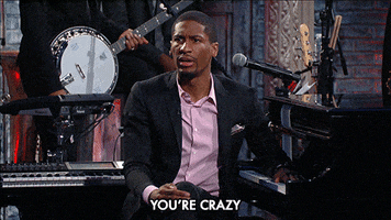 TV gif. Jon Batiste on The Late Show With Stephen Colbert looks angry as he leans on the piano while pointing and saying, "You're crazy!"