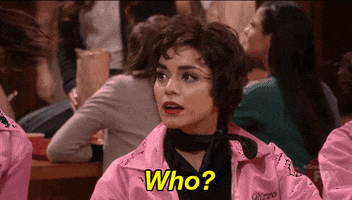 TV gif. Vanessa Hudgens as Rizzo in Grease Live sits on a bench at lunch time. She looks over to her left and sarcastically says, “Who?”