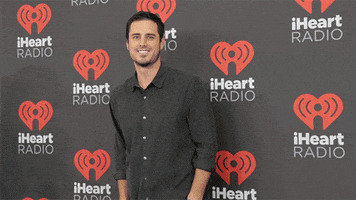Celebrity gif. Ben Higgins is on the red carpet at the iHeartRadio Festival and he waves at us and smiles charmingly.