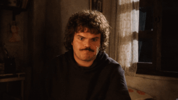 Movie gif. Jack Black as Nacho from Nacho Libre makes a bitter face at us, then speaks, looking around carelessly. Text, "Whatever."
