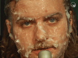 Video gif. A man stares at us with a microphone close to his mouth. His whole face is thickly covered with vaseline. He has a serious expression on his face as he says, “please.”