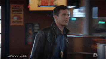TV gif. Andy Samberg as Jake Peralta on Brooklyn Nine-Nine goes up to a bar and without even looking at him, high fives Joe Lo Truglio as Charles Boyle. Charles does a small spin as he high fives Jake.