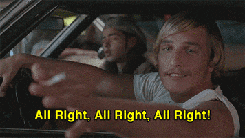 Movie gif. Actor Matthew McConaughey in Almost Famous sits behind the wheel of a car and gestures with the cigarette in his hand. Text, "All right, all right, all right!"