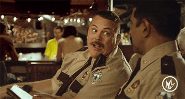 Movie gif. In a restaurant, Kevin Heffernan as Mac in Super Troopers leans over and smiles as he playfully pokes Thorny, played by Jay Chandrasekhar.