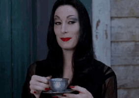 TV gif. Morticia Addams from the Addams Family sips a cup of tea with a mysterious smile on her face.