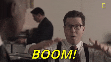 TV gif. From Valley of the Boom, man with slicked-back hair and glasses, wearing a striped shirt with suspenders, makes a mushroom-cloud explosion gesture with his hands and says "Boom!" which appears as text.