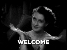 Movie gif. In a black-and-white scene from the 1931 film A Free Soul, a smiling Norma Shearer as Jan awaits us with outstretched arms, and holds the same pose as she wiggles her fingers. Text, "Welcome."