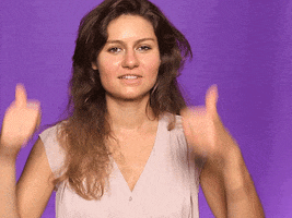 Video gif. Woman looks at us with a smile grin and holds two big thumbs up towards us.