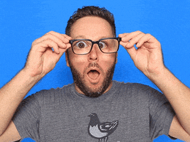 Video gif. A man holds his glasses out away from his eyes, magnifying them as if in amazement. 