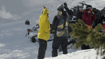 Video gif. Two men in snowboarding gear stand in the snow and give each other a big high five.