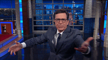 Late Show gif. Stephen Colbert reaches out to us with an open hand on set and says, "Welcome."