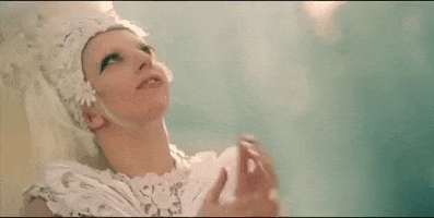 Music video gif. In the video for G.U.Y., dressed in a white floral headdress and dress, Lady Gaga looks hopefully heavenward and clasps her hands together.