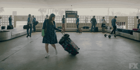 A gif image of a woman struggling with a suitcase as she leaves baggage claim at the airport.