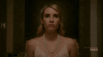 TV gif. Emma Roberts as Chanel Oberlin in Scream Queens stands up from the dining table defiantly, pointing her finger and spitting “how dare you.”