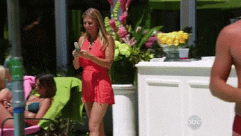 Video gif. Woman walks into a pool while texting and continues to text while floating.