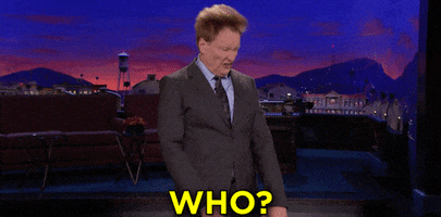 Late Night gif. Conan O'Brien as host stands on stage and angrily nods his head back and forth, flipping his hair around, as he screams, "Who?"