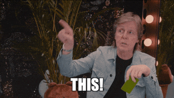 Celebrity gif. Paul McCartney looks at us, holding a card in one hand, and pointing up in the air. Text, “This!”