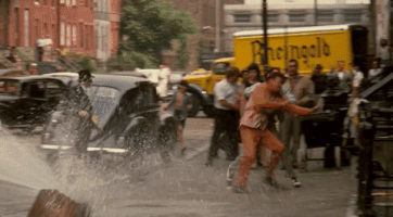 Movie gif. On a crowded street, James Caan as Sonny in The Godfather throws Gianni Russo as Carlo over a metal railing, hops over it and then starts punching Carlo.