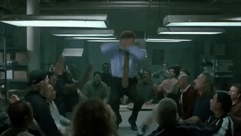 Movie gif. Will Ferrell as Buddy the Elf in Elf dances on a table surrounded by cheering office workers. 
