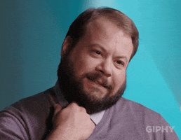 Video gif. Bearded man wears a gray pullover sweater over a collared shirt, which he tugs at uncomfortably. He gazes awkwardly to the right, as if he's trying to escape the situation.