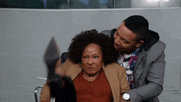 TV gif. Wanda Sykes as Daphne in Blackish kicks her legs in the air as if ready for a fight as a man restrains her. 