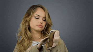 Celebrity gif. Debby Ryan is using 2 mini hands to hold a phone and she swipes right while looking intrigued then swipes again and looks appalled.