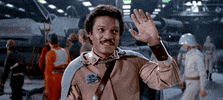 Star Wars gif. Billy Dee Williams as Lando in Star Wars: Return of the Jedi. He's bidding someone farewell and gives them a proud smile while tipping two fingers at them, wishing them well. 