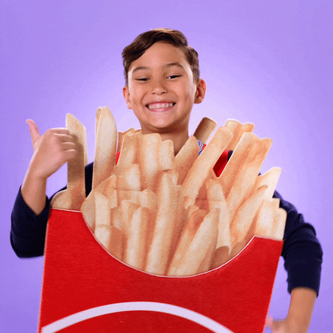 Video gif. Child smiles and dances with thumbs up, dressed in costume as a carton of french fries.