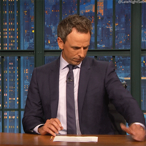 Late Night gif Holding an imaginary phone Seth Meyers scrolls and then stops looking annoyed and rolling his eyes dramatically