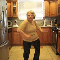 Video gif. Older woman silly-dances in her kitchen, then is joined by two other women doing the same.