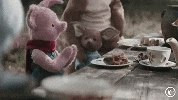 Movie gif. At a picnic table with Kanga, Roo, and others, Piglet from Christopher Robin smiles and claps his hands while glancing around.
