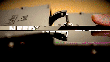 Video gif. Finger pokes at a metal lever on a black box that opens up to reveal a stick that pokes the lever back when the finger moves it. The video has a glitch effect over it. Text, “I need this in my life.”