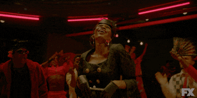 TV gif. Dominique Jackson as Elektra Abundance in Pose, reveling in applause and cheers from the crowd encircling her, theatrically fanning herself off.