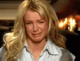 Celebrity gif. In an interview scene, Britney Spears slouches into her chair, crying, covering her face with her hands.
