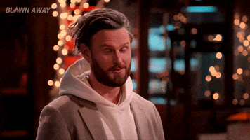 Reality TV gif. Bobby Berk on Blown Away raises an eyebrow and turns his head as if interested. 