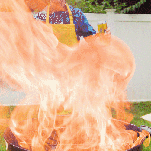 Video gif. Man wearing a yellow apron and holding a spatula stands behind a round outdoor grill. Flames burst from the grill into the air. 