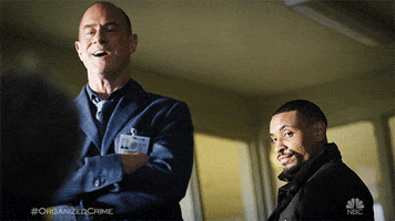 TV gif. Christopher Meloni as Elliot Stabler on Law & Order Organized Crime, arms crossed looking down at someone, laughs out sarcastically, a man beside him nodding, serious.